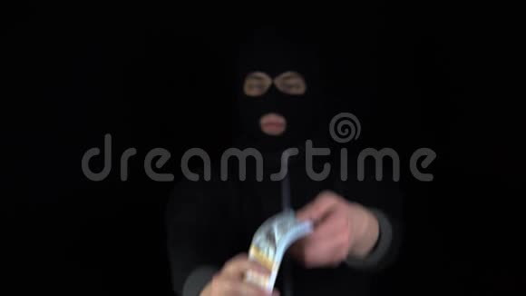 一个戴着巴拉克拉瓦面具的人拿出一大笔钱班迪特通过钱在黑色的背景上视频的预览图