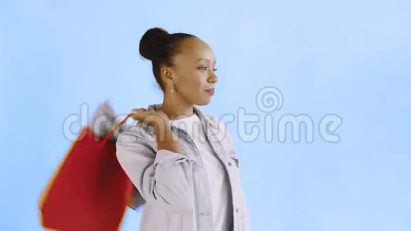 非洲裔美国妇女带着购物袋的肖像正在工作室的蓝色背景上喝咖啡琼夹夹克视频的预览图