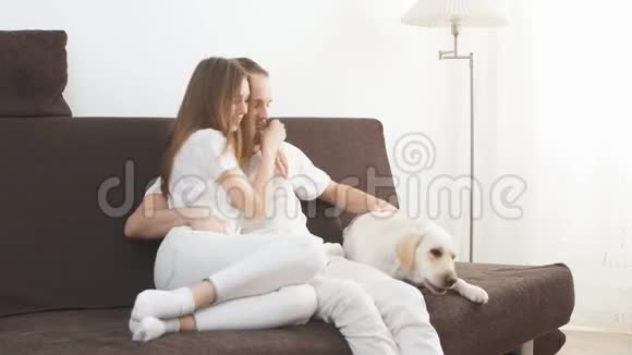 可爱的白种人夫妇和他们的宠物白狗坐在沙发上视频的预览图