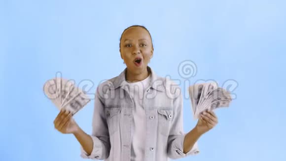 满意的兴奋的兴奋的非裔美国妇女在蓝色背景的让夹克上展示金钱说上帝的上帝视频的预览图