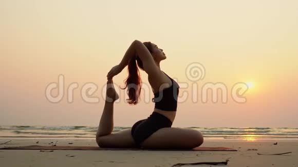 在沙滩和沙滩上放松瑜伽王鸽姿势的女性慢动作视频的预览图