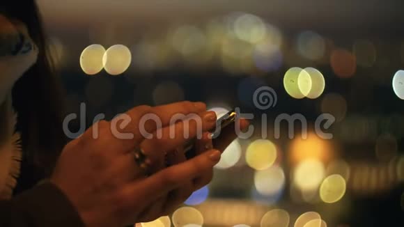 超级特写女性手使用智能手机购物应用程序在惊人的bokeh日落城市灯光背景慢运动视频的预览图