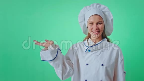 漂亮的女人面包师在一个绿色的工作室墙上直视着相机微笑着大举起手保持不变视频的预览图