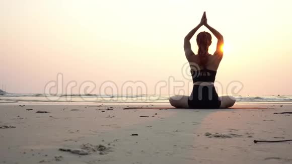 背面的观点女人练习瑜伽莲花姿势冥想与暑假在海滩上视频的预览图