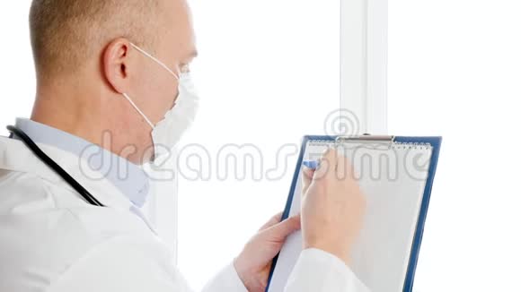 男医生穿着白色外套和防护面罩在医院的剪贴板上写冠状病毒穿着医用礼服的病毒学家视频的预览图