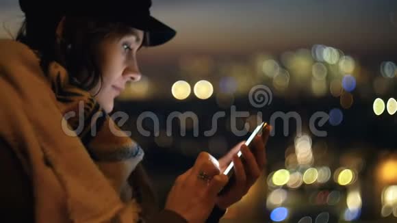 美丽的年轻女子在史诗般的日落城市景色的社交网络上发帖她的脸被屏幕缓慢的动作照亮视频的预览图