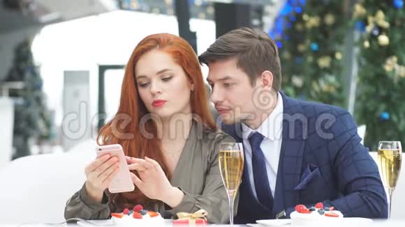 一对情侣在餐馆里浪漫约会浏览红发女孩智能手机上的在线菜单视频的预览图