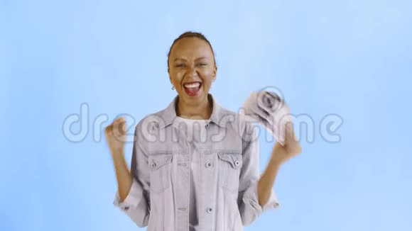 满意的兴奋的兴奋的非裔美国妇女在蓝底Jean夹克上展示金钱和相机跳舞视频的预览图