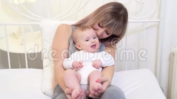 妈妈亲吻坐在床上的婴儿头视频的预览图