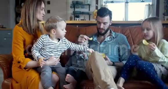 快乐轻松的家庭时光在家年轻的白种人妈妈爸爸和三个孩子坐在一起吃零食慢动作视频的预览图