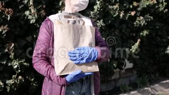 食品配送年轻妇女戴着防护面罩和手套携带来自商店的产品流行病视频的预览图