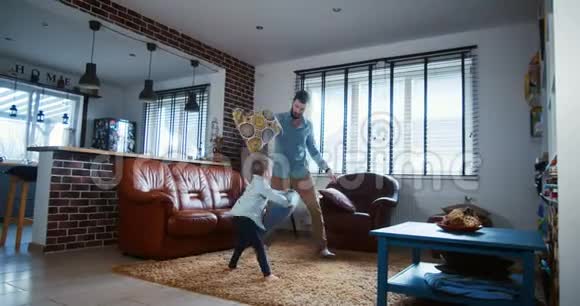 快乐的年轻白种人父亲和小儿子玩耍打架枕头在现代轻屋客厅慢动作视频的预览图