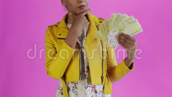 体贴成功的非裔美国妇女与金钱爱好者粉红色背景在工作室黄色夹克视频的预览图