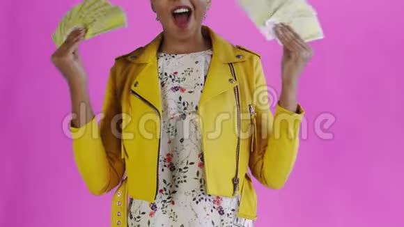 心满意足高兴兴奋的非洲裔美国妇女在粉色背景黄色夹克上炫耀金钱并说上帝啊视频的预览图