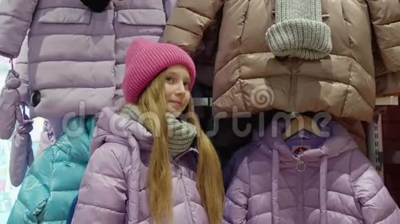 年轻女孩在购物时在时装店里试羽绒服快乐的年轻女孩在购物时展示新的羽绒服视频的预览图