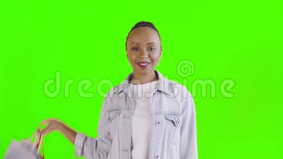 美国黑人妇女带着购物袋的肖像在工作室的绿色背景上竖起大拇指琼夹夹克视频的预览图