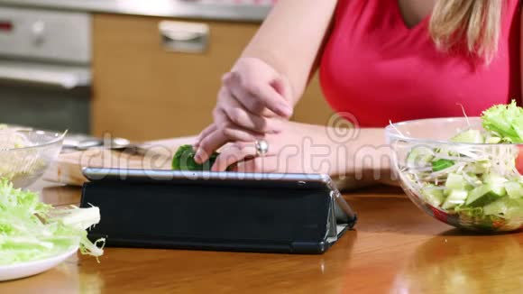 一位年轻女性用数码平板电脑在网上阅读食谱准备沙拉的手视频的预览图