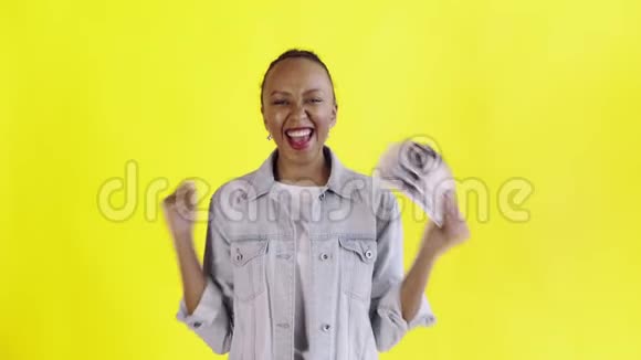 满意的兴奋的兴奋的非裔美国妇女在黄色背景的Jean夹克上展示金钱和相机跳舞视频的预览图