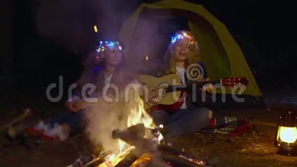 晚上妈妈和女儿在露营地用吉他前篝火演唱歌曲女儿一起玩音乐唱歌视频的预览图