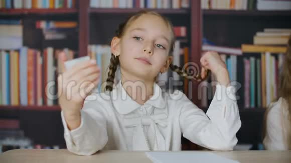 可爱的学校女孩带着辫子看着小镜子在教室里摸着头发肖像女学生搞笑视频的预览图