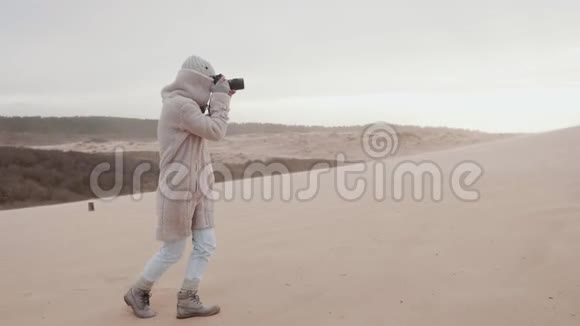 快乐职业女摄影师挣扎着在极端风慢动作下拍摄沙丘海滩的照片视频的预览图