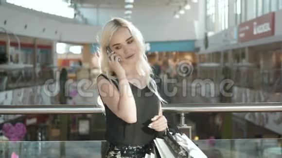 快乐的金发女郎在购物中心使用手机美丽的学生女孩在购物中心购物视频的预览图
