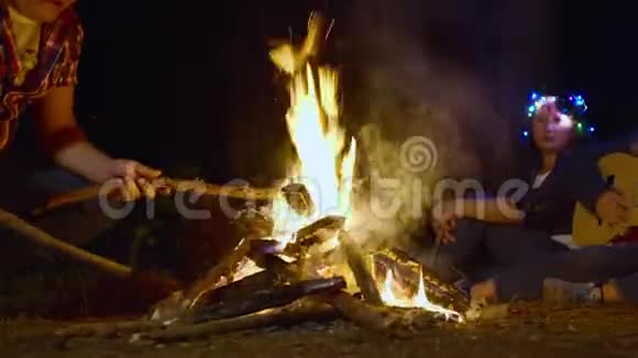 在露营旅行中男人把木柴放在燃烧的篝火里游客燃烧篝火用吉他唱歌视频的预览图