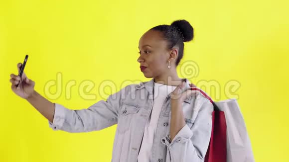 美国黑人妇女带着购物袋的肖像正在工作室的黄色背景上自拍琼夹夹克视频的预览图
