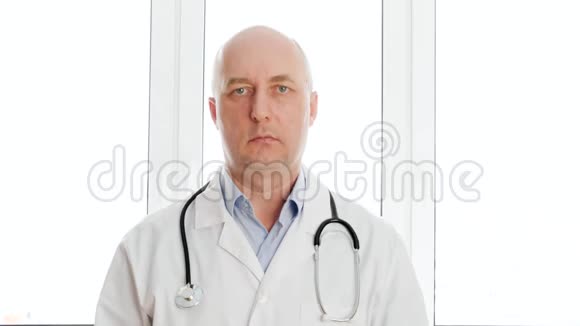 男医生穿着白色医用长袍带音响镜在窗口背景上看相机肖像医疗工作者视频的预览图