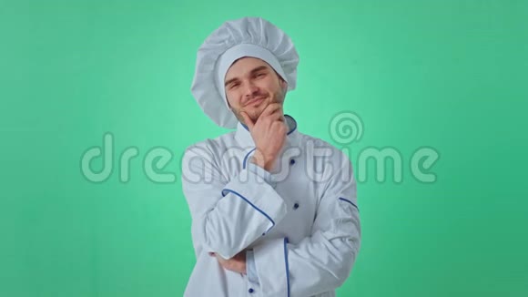 穿着制服摸着下巴绿色背景墙的有魅力的面包师男子直视着摄像机视频的预览图