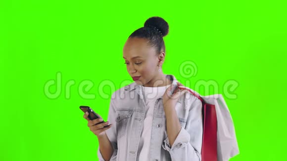 美国黑人妇女带着购物袋的肖像是在工作室的绿色背景上通过智能手机谈论的让视频的预览图