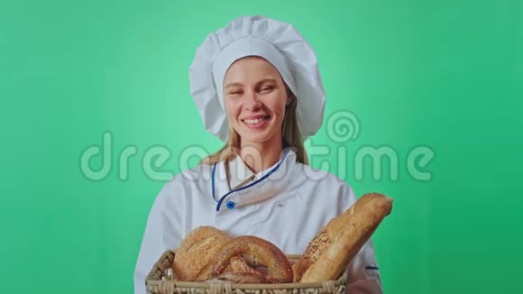 女面包师带着美丽的微笑手里拿着一篮子新鲜面包她直视着镜头绿色工作室视频的预览图