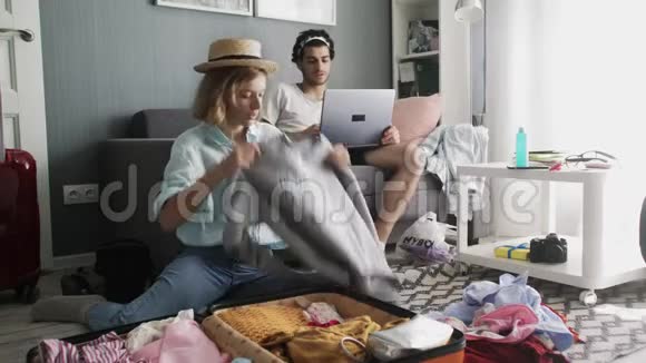 沙发上有笔记本电脑的人和戴帽子的女孩把衣服放进手提箱准备旅行视频的预览图