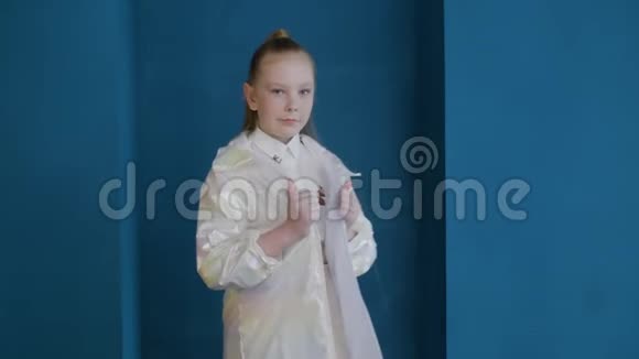 少女模特穿着白色夹克在蓝墙背景上摆姿势穿着时髦白大褂的时尚少女视频的预览图