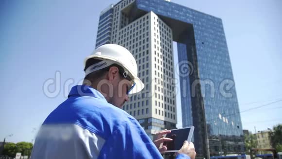 一位成功的年轻英俊工程师建筑师建筑工人商人的肖像戴着白色头盔手持一个视频的预览图