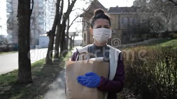 食品配送年轻妇女戴着防护面罩和手套携带来自商店的产品流行病视频的预览图