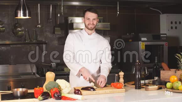 年轻的厨师在现代餐厅的厨房里用木板茄子切片视频的预览图