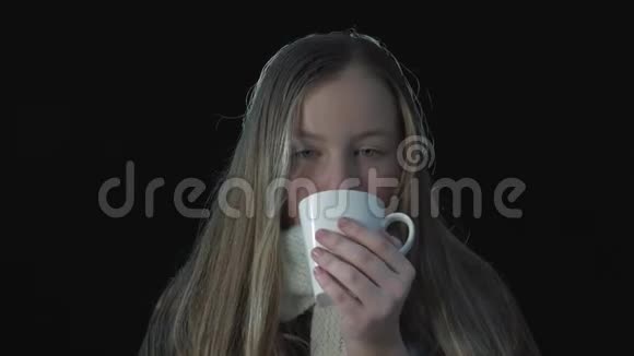 可爱的女孩想取暖在黑色背景下喝着热饮捧着杯子微笑着可爱视频的预览图