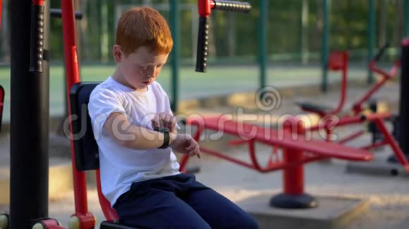 街上一个男孩在公共健身器材上看手表视频的预览图
