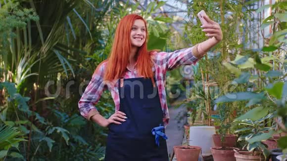 漂亮的花匠红发女郎带着大大的微笑她用智能手机在中间拍了几张照片视频的预览图