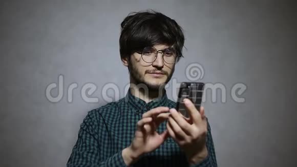 年轻人使用智能手机戴眼镜和绿色衬衫的肖像视频的预览图