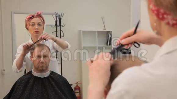 理发师是一个漂亮的金发女郎头带着一个别针把一个男人头发剪在椅子上她完成理发过程视频的预览图