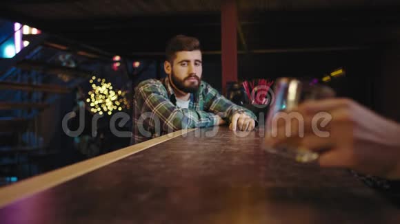 在酒吧里一个年轻人在酒吧桌上等着他的饮料酒保给顾客一杯饮料他很高兴他开始了视频的预览图