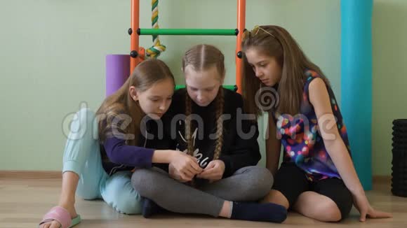 三个女生在体育课上休息时使用手机十几岁的女朋友坐在地上看着智能手机视频的预览图
