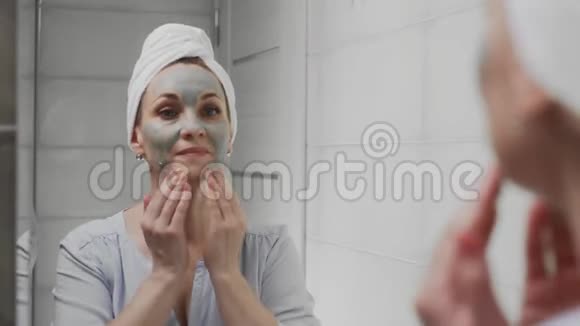 成年妇女头上戴着毛巾脸上戴着黏土面具看着镜头视频的预览图