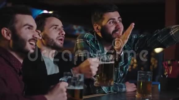 在酒吧里好朋友从啤酒杯里喝啤酒在电视上观看他们最喜欢的集中比赛他们尖叫和视频的预览图