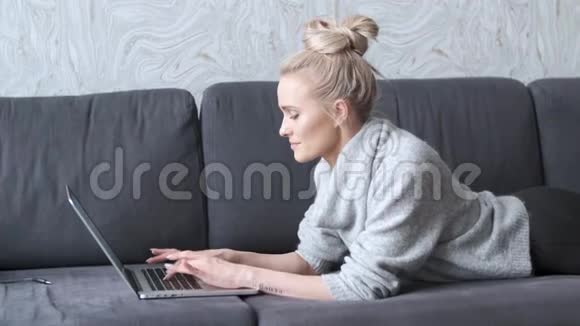 快乐的金发女人躺在沙发上手提电脑视频的预览图