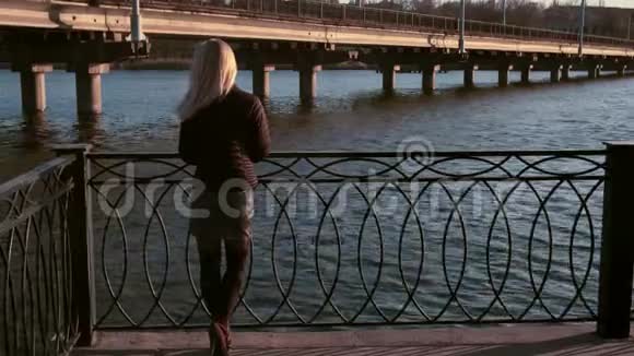 阳光明媚的日子美丽的年轻女子站在河堤上视频的预览图