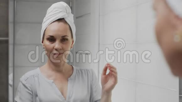 成年妇女头上戴毛巾涂奶油照镜子享受自然的美丽和健康视频的预览图