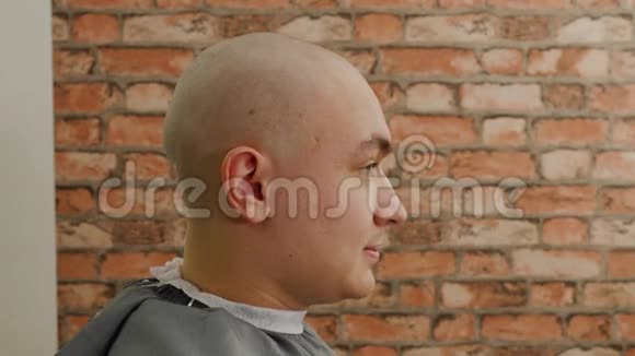 光头男坐在男发廊的理发椅上理发店刮胡子后的秃头视频的预览图